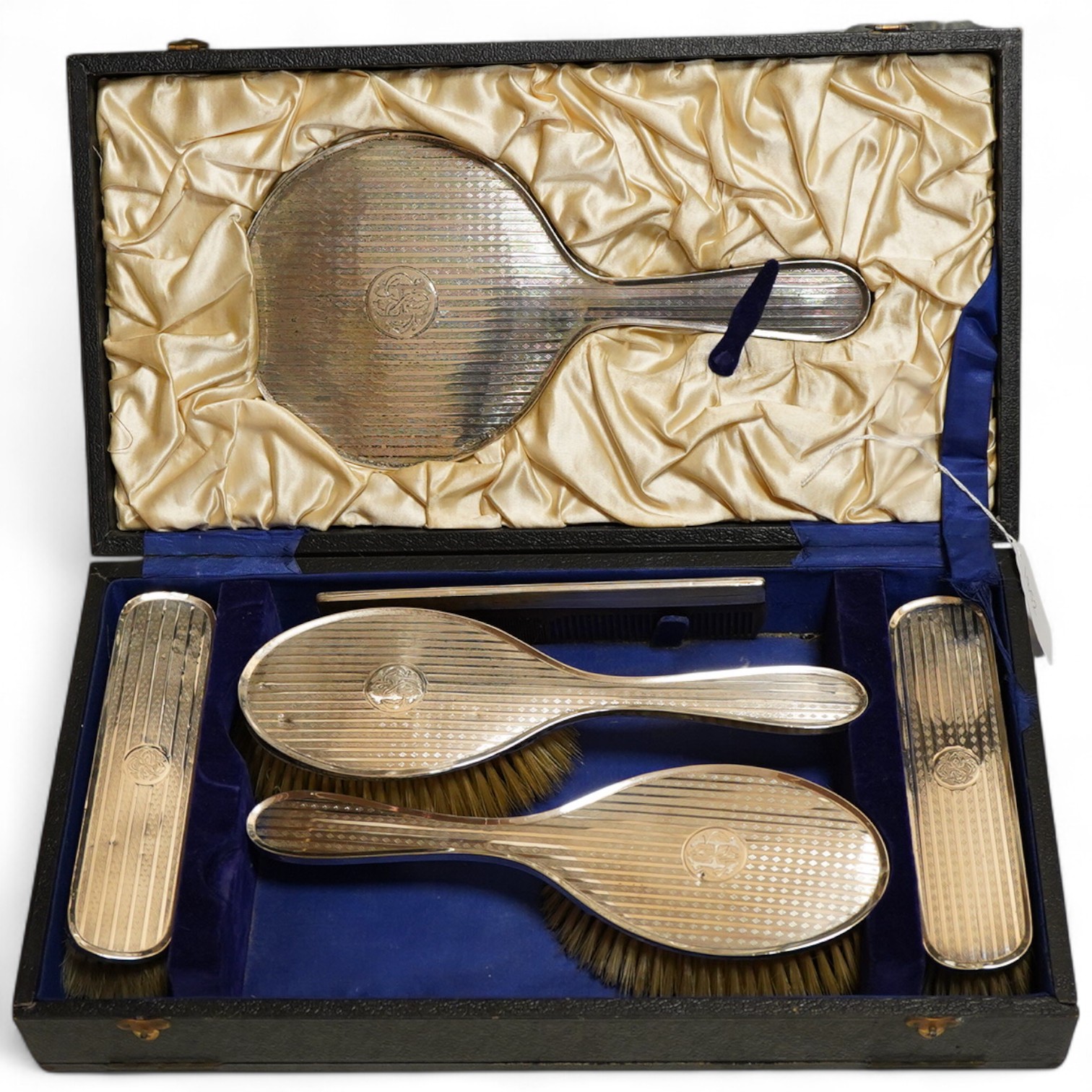 A George V silver six piece engine turned dressing table set Birmingham, 1922 Carringon & Co, comprising hand mirror, pair hairbrushes, pair clothes brushes and a mounted tortoiseshell comb, initialled, in a fitted case